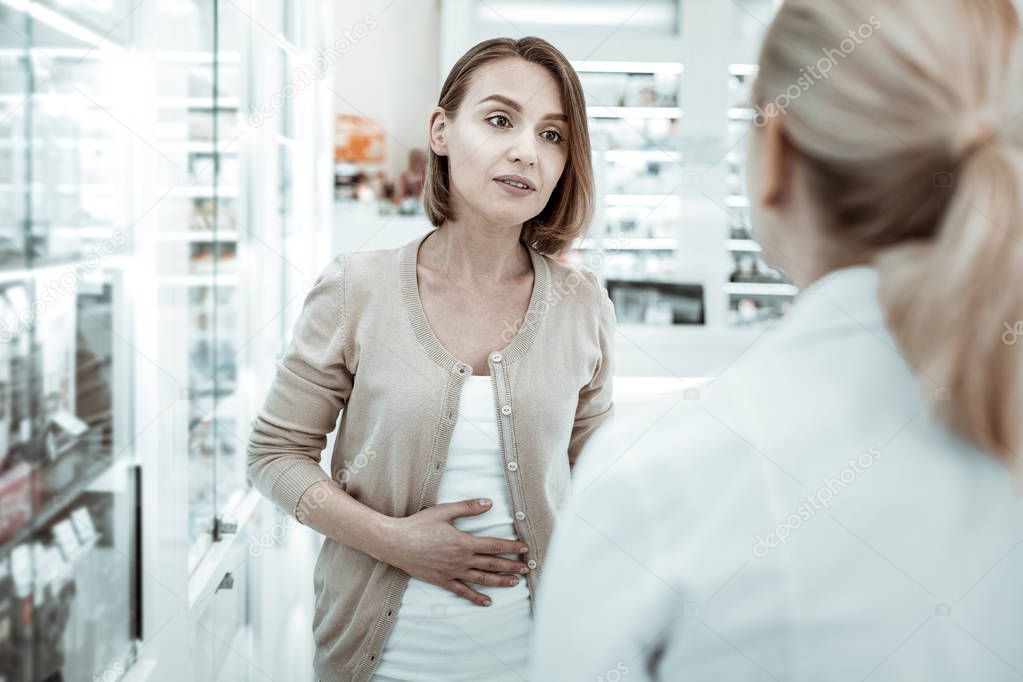 Attractive woman complaining to the druggist of her stomach ache.