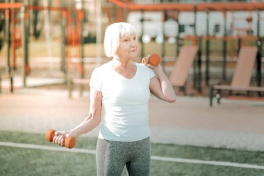 Yaşlılar için spor. Spor yaşlı mutlu görünümlü bayan açık ağırlıkları ile kollar için fiziksel bir egzersiz yapıyor atletik giyim giyiyor.