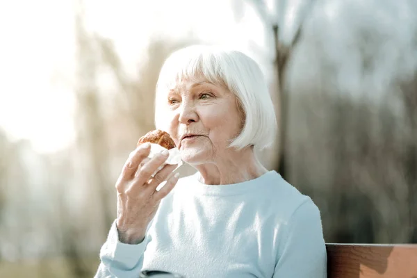 Agradável sorrindo madame envelhecido saboreando de um delicioso pão ao ar livre — Fotografia de Stock