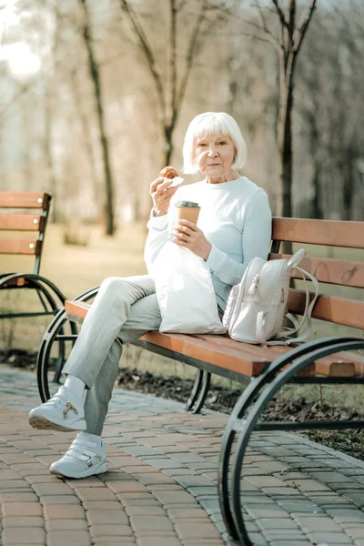 Захватывающее сияние пожилой женщины, которая ест печенье и пьет кофе. — стоковое фото