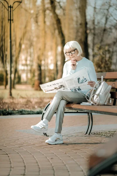 ベンチで思慮深く新聞を読む眼鏡で快適な超年金女性 — ストック写真