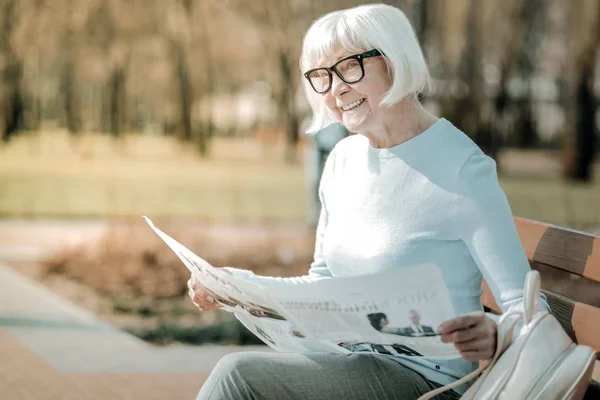 Энергичная стареющая женщина с хорошим вкусом читает новости с улыбкой — стоковое фото