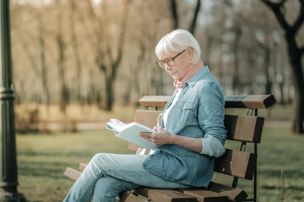 Prebesitter äldre fru i glasögon läsa uppmärksamt en bok — Stockfoto