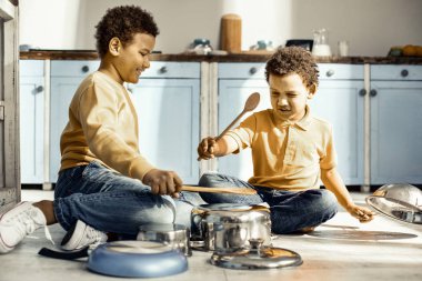 Mutfak zemininde oturan ve yaratıcı kaynaklarla oynayan çocuklar.