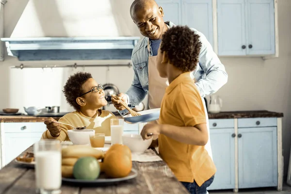 En la cocina bañada por el sol un hombre y sus dos hijos comiendo y charlando . — Foto de Stock