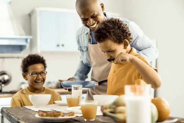 Niño probando la comida que se prepara, su padre y su hermano riéndose . —  Fotos de Stock