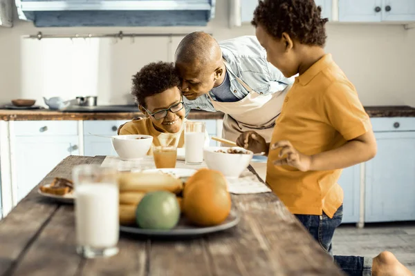 Man in apron in turns hugging his sons. — Stock Photo, Image