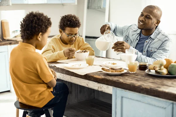 Hermanos sentados a la mesa esperando que papá les sirva la leche. . —  Fotos de Stock