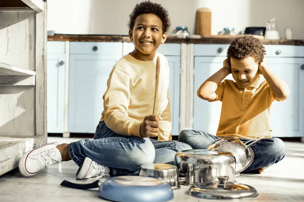 Хлопчик прикриває вуха, а його брат намагається грати на посуді . — стокове фото