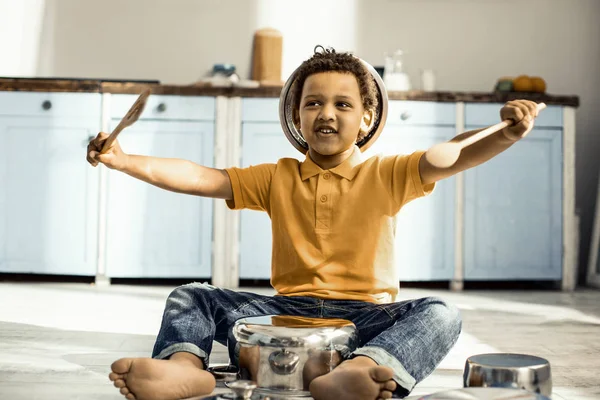 Kid sitting on the kitchen floor and knocking on the dishes with spoons. — Stock Photo, Image