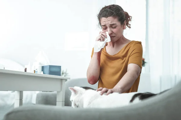 Жена сидит на диване с сильной аллергией на кошек и пыль — стоковое фото