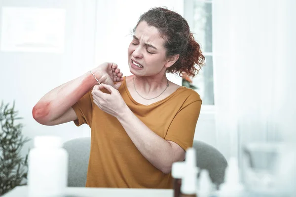 Krullend vrouw nemen armband uit terwijl het hebben van uitslag op pols — Stockfoto