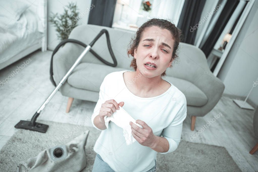 Curly woman sneezing in living room having allergy to dust