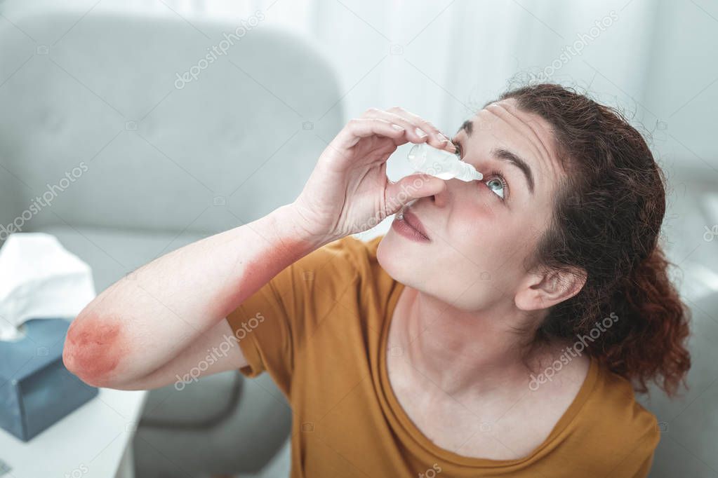 Curly red-haired woman dropping her eyes having allergy