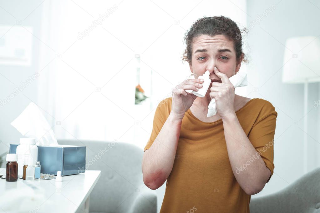 Curly woman wearing orange shirt using nose spray having allergy
