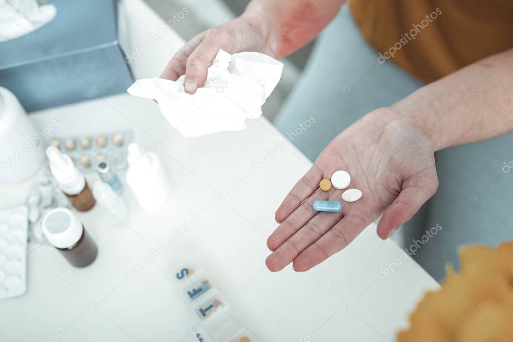 Woman holding pills and napkin while suffering from allergy