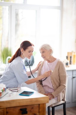 Yaşlı bayanı ziyaret ederken stetoskop kullanan sağlık görevlisi