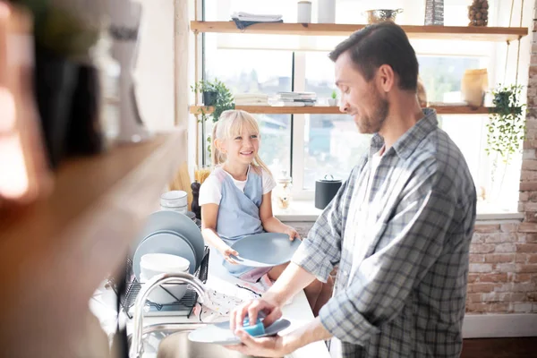 Datter smiler og snakker med pappa, vasker opp – stockfoto