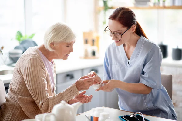 Verzorger dragen van glazen geven vitaminen aan leeftijd dame — Stockfoto