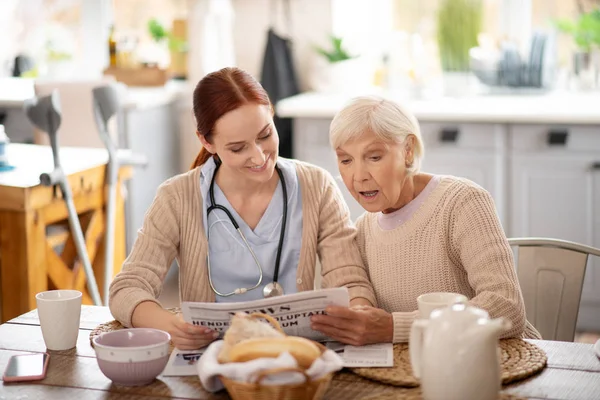 Ο φροντιστής διαβάζει τα πρωινά νέα για συνταξιούχος γυναίκα — Φωτογραφία Αρχείου