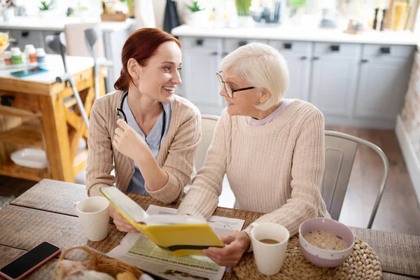 Mujer y cuidador tomando té y leyendo — Foto de Stock