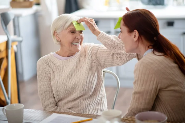 Cuidador pelirrojo bromeando y divirtiéndose con una anciana — Foto de Stock