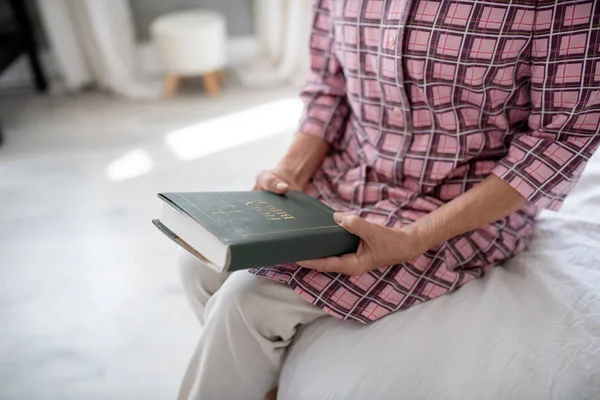 Pensioner wearing checked shirt holding Holy Bible