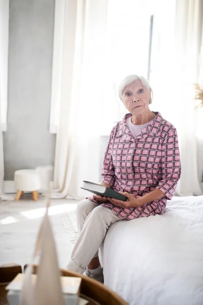 Сіроволоса жінка сидить у спальні з книгою — стокове фото