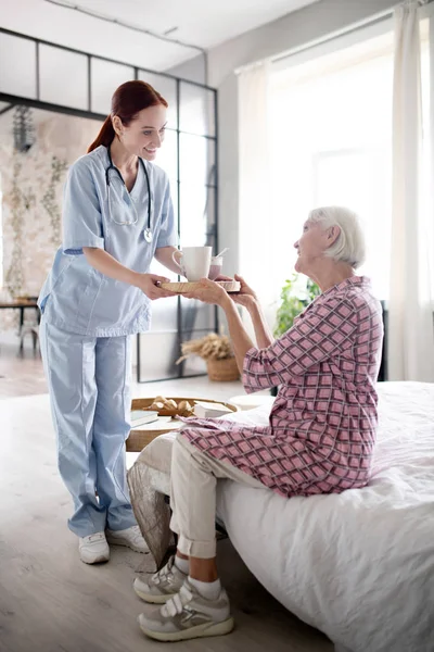 Infirmière souriante tout en donnant le petit déjeuner à une femme âgée — Photo