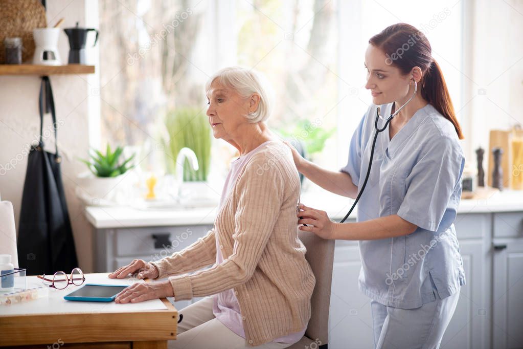 Retired woman sitting still while nurse examining her
