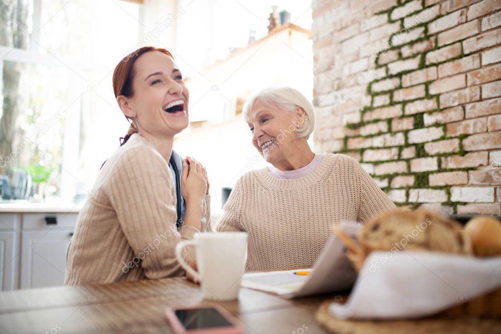 Red-haired caregiver laughing while pensioner joking