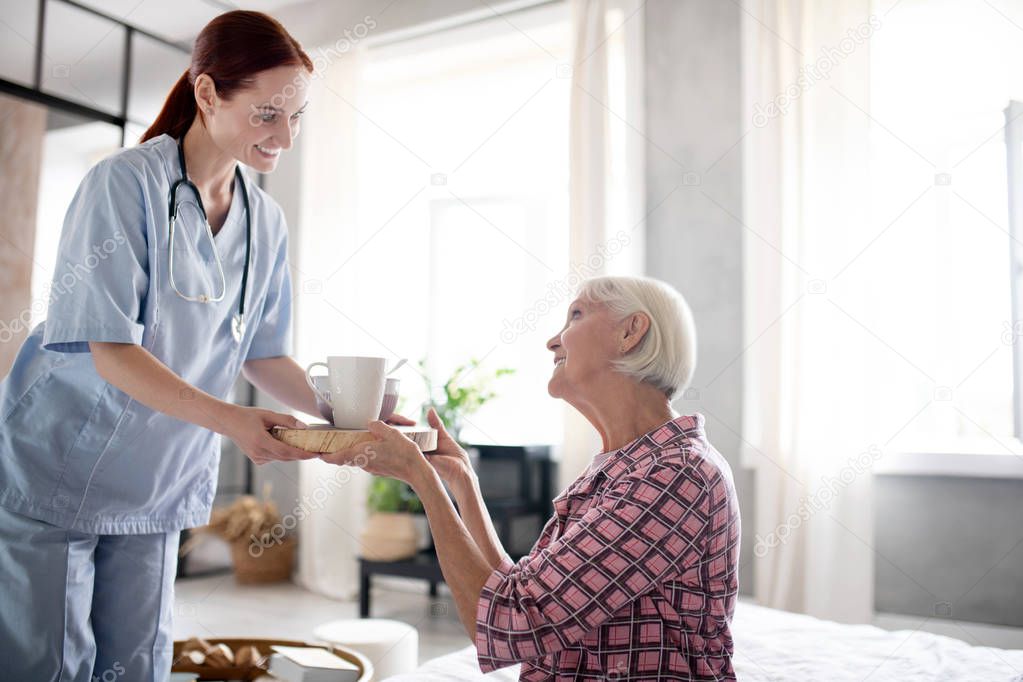 Red-haired nurse bringing breakfast for retired woman