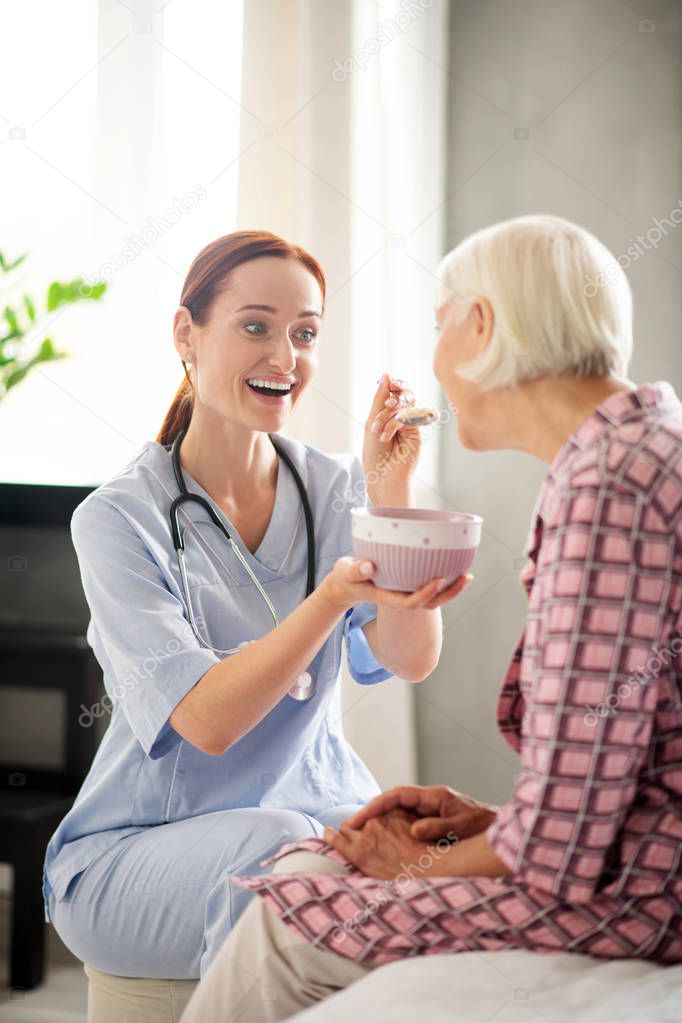 Caregiver feeding retired woman while giving her oatmeal