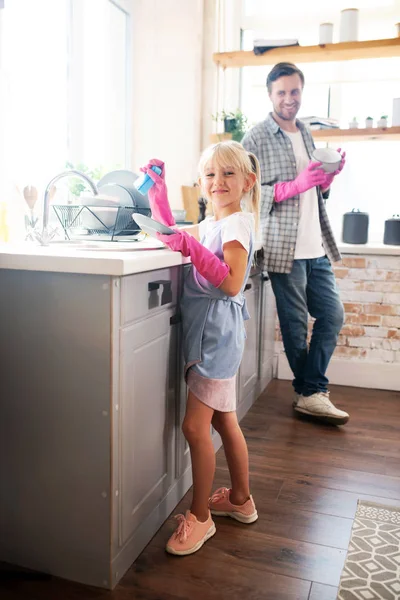 Preciosa hija con guantes rosas lavando los platos —  Fotos de Stock