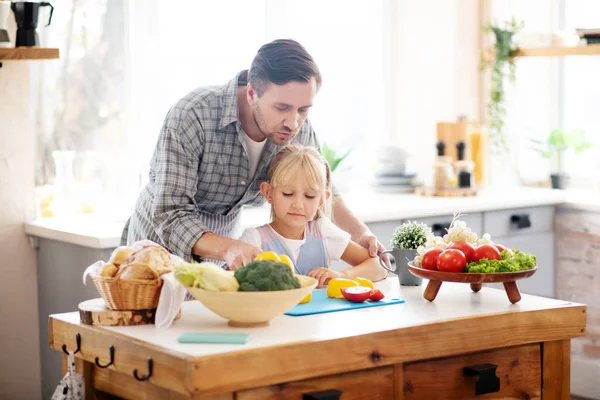 Father helping daughter to use knife while cutting vegetables — Stock Photo, Image