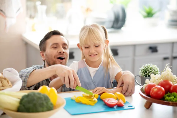 Blonde daughter smiling while cutting peppers with daddy — Stock Photo, Image