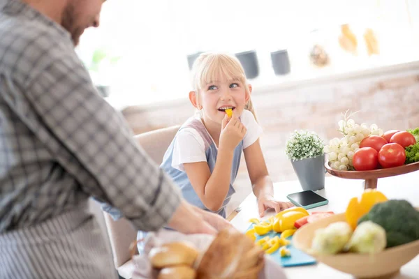 Cute daughter biting some pepper while cooking with daddy — Stock Photo, Image