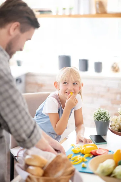 Hija comiendo pimienta mientras padre cocinando el almuerzo —  Fotos de Stock