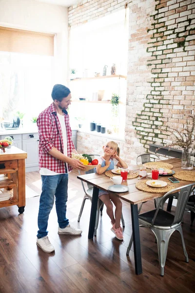 Daddy bringing vegetables for daughter while having breakfast