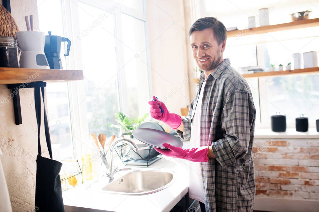 Husband wearing pink gloves smiling and washing the dishes