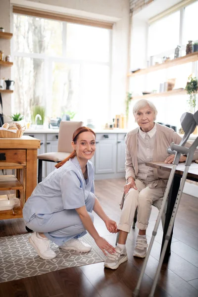 Aide soignant souriant tout en aidant la femme âgée à dentelle chaussures — Photo