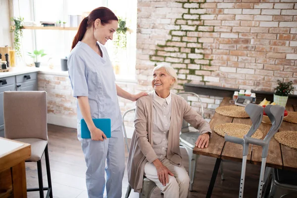 У віці жінка розмовляє з її корисною старанною медсестрою — стокове фото