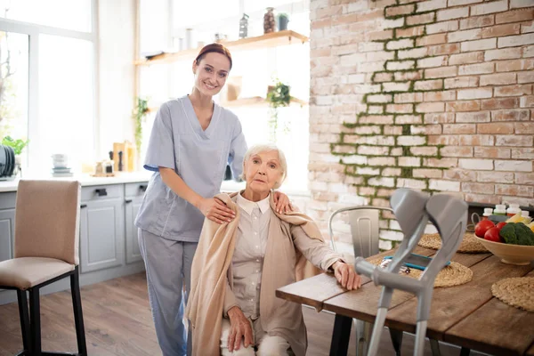 Helpful red-haired nurse standing near aged woman
