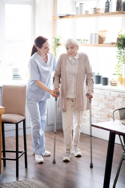 Verzorger assistente vrouw wandelen met krukken — Stockfoto