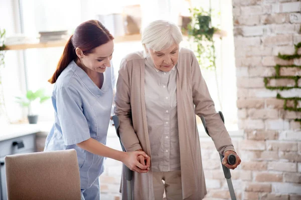 Helpful caregiver assisting woman with crutches — Stock Photo, Image