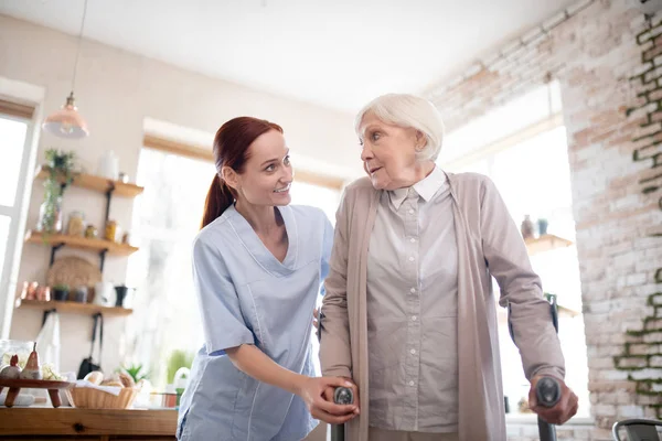 Red-haired caregiver supporting woman with crutches — Stock Photo, Image