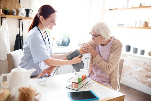 Sjuksköterska mäter tryck för gråhårig pensionär — Stockfoto