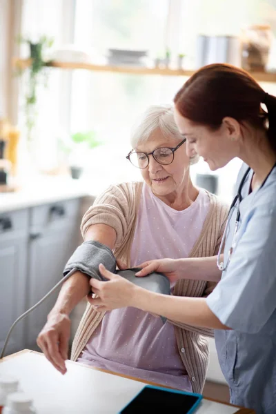 Retired woman watching nurse measuring blood pressure