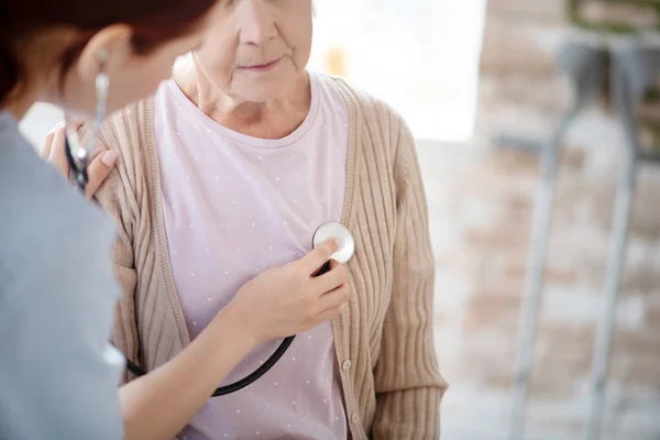Enfermeira cuidadora usando estetoscópio enquanto examina a mulher aposentada — Fotografia de Stock