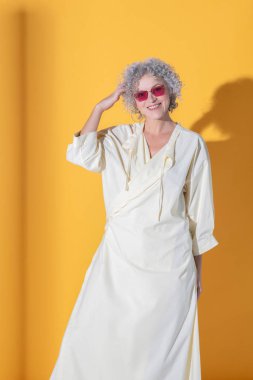 Uzun beyaz elbise giyen kıvırcık kadın gülümsüyor.